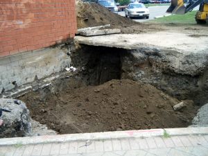 A large hole under a home exposes a mound of soil as foundation and basement underpinning takes place.