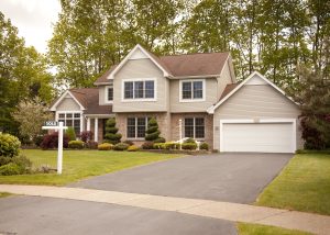 Front view of a two-floor, brick-and-siding suburban home with trees behind it and a small SOLD sign on the front lawn.